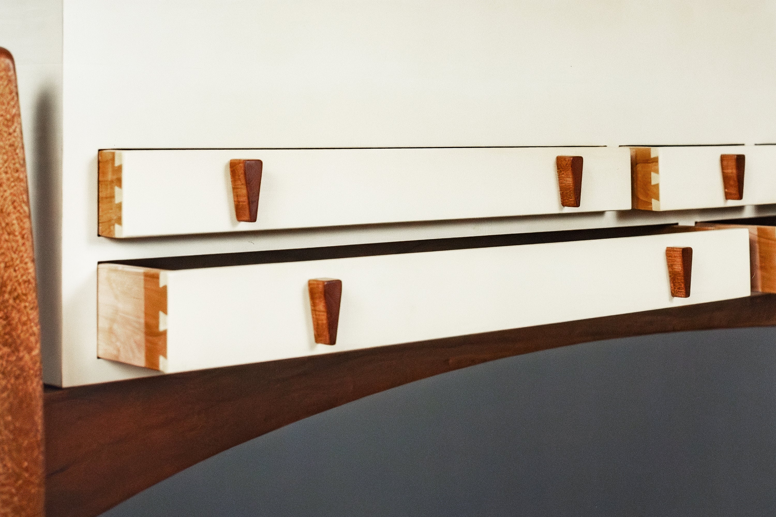 Close-up of a mid-century modern wooden drawer unit with white drawer fronts, warm brown wood drawer pulls, and visible dovetail joint construction.