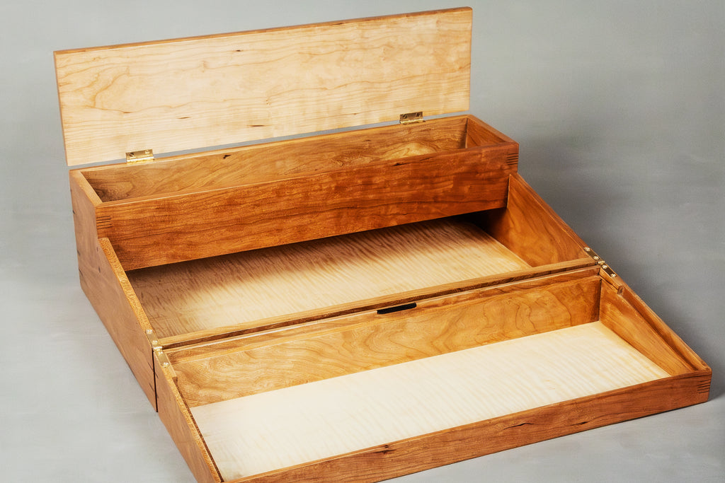 An open wooden storage box with a hinged lid and two nested compartments, made from light-colored wood with visible grain, photographed against a neutral gray background.