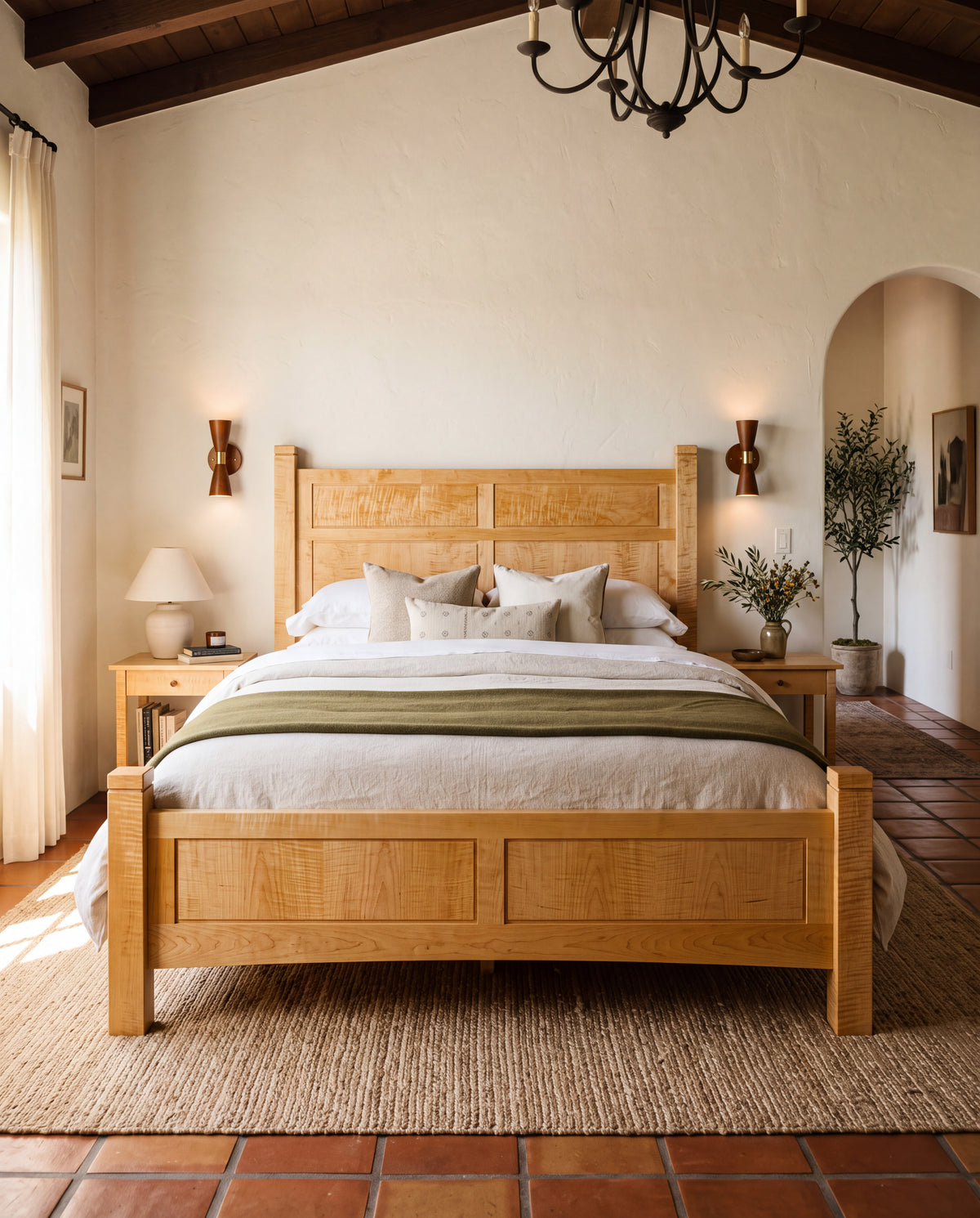 A rustic light curly maple wooden bed frame with a slatted headboard and footboard, styled in a warm, rustic bedroom with terracotta tile floors, a woven jute rug, and a black chandelier. custom furniture