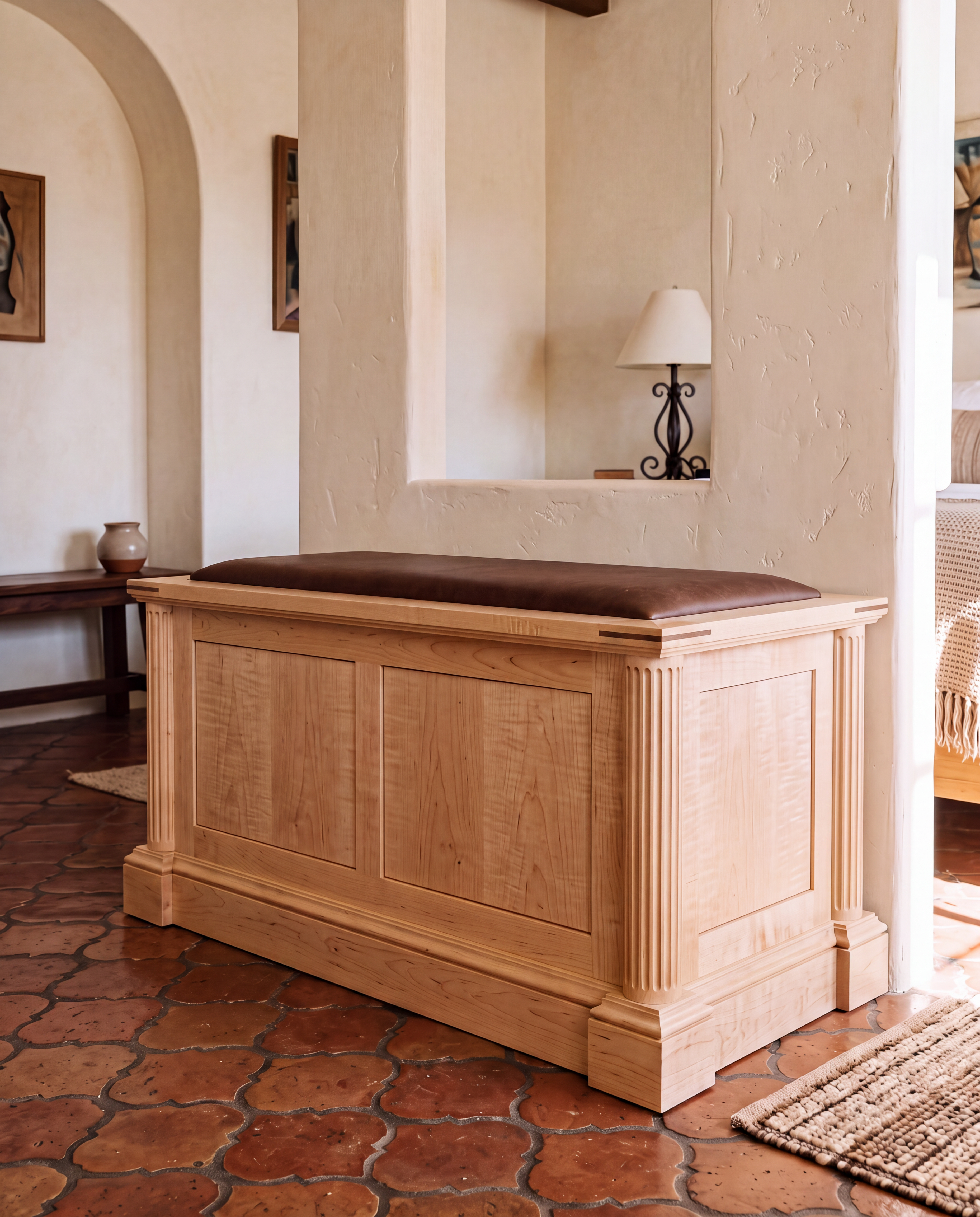 A light natural wood entryway storage bench with a dark brown upholstered cushion, set in a rustic home interior with terracotta tile flooring and textured cream walls.